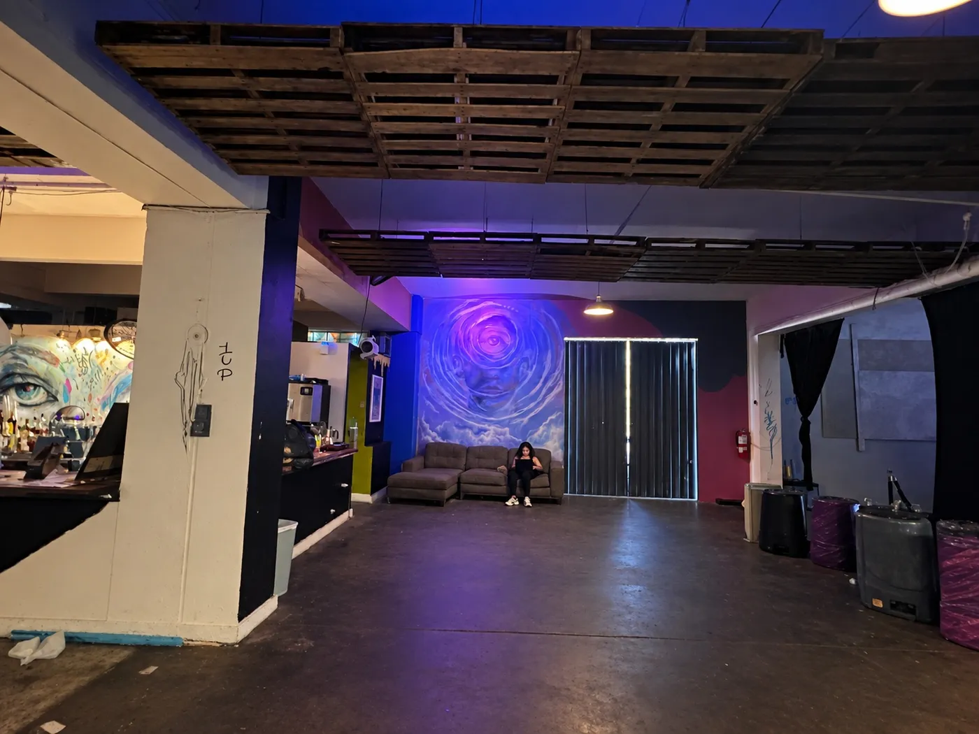 Salón amplio con techo de paletas de madera y el mural de un ojo al fondo