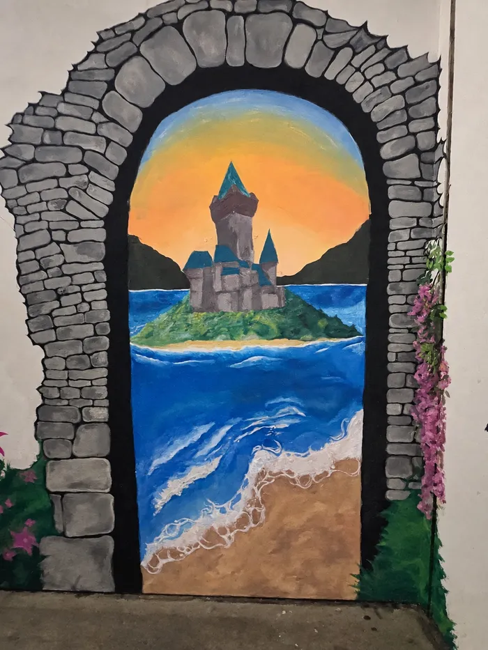 Mural de un arco de piedra que se abre a un castillo en una isla y una playa