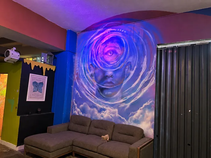 Mural de un rostro envuelto en remolinos azules sobre un sofá gris