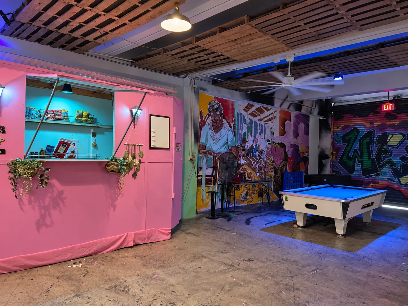 Área recreativa con mesa de billar, una ventanilla rosada y murales
