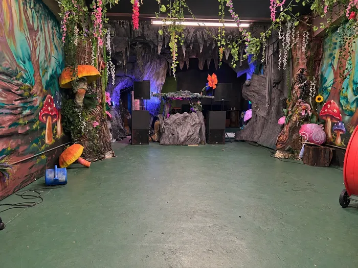Vista completa del Forest Room con piso verde, troncos esculpidos y la cabina en una cueva