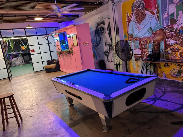 Mesa de billar bajo luz violeta junto al mural de una mujer mayor
