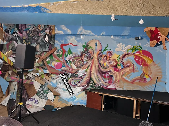 Mural de un pulpo junto a la tarima del Q Floor, con una bocina en trípode